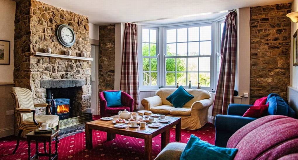 The cozy reception room at Ross Lodge Gloucestershire with a stone fireplace and colorful seating, providing a warm communal space for the group that sleeps 26.