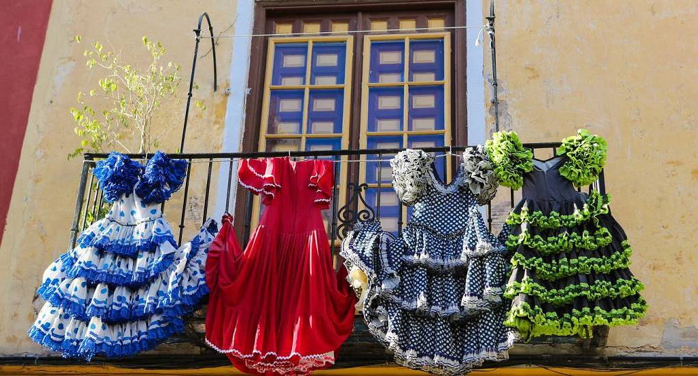 Ruffled Spanish flamenco dresses hanging on a balcony railing, colorful cultural backdrop for a Seville hen do.