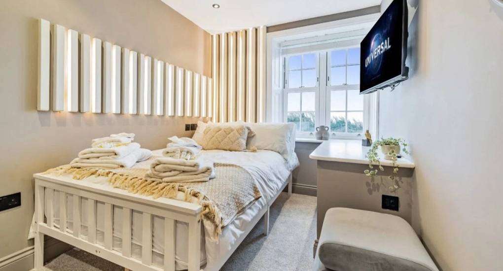 Off white decorated bedroom with single bed made up and wall mounted tv