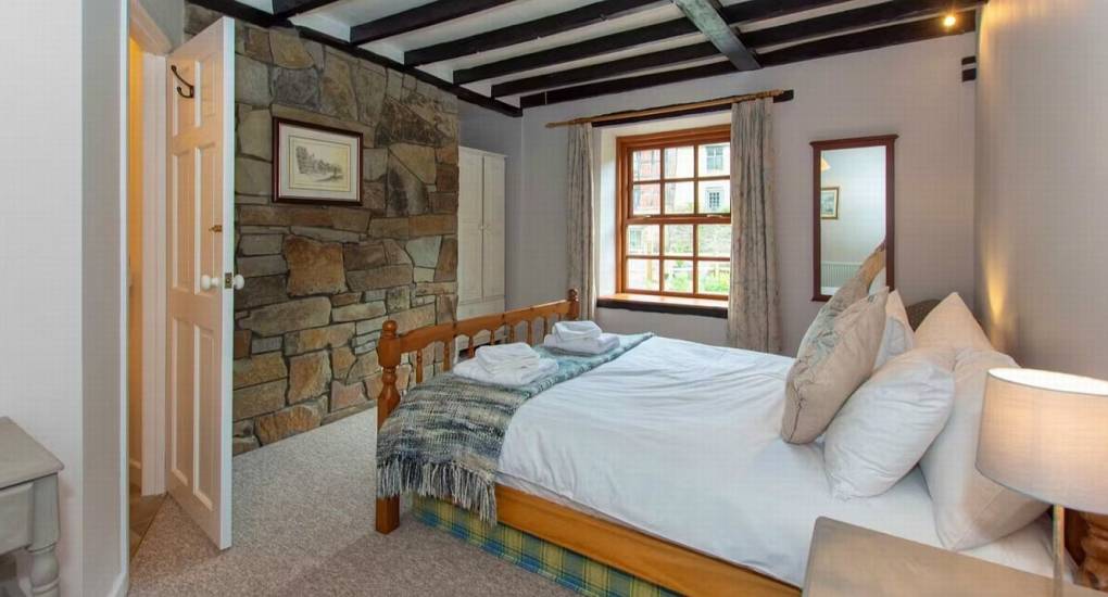 A stylish double bedroom at Standing Barn Gloucestershire with a rustic stone feature wall and wooden ceiling beams, part of the unique design of this Gloucestershire Party House.