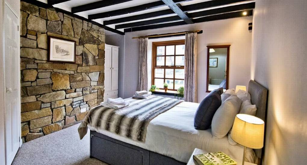 A luxurious double bedroom at Standing Barn Gloucestershire with exposed stone walls and dark ceiling beams, offering stylish sleeping for the party house that sleeps 22.