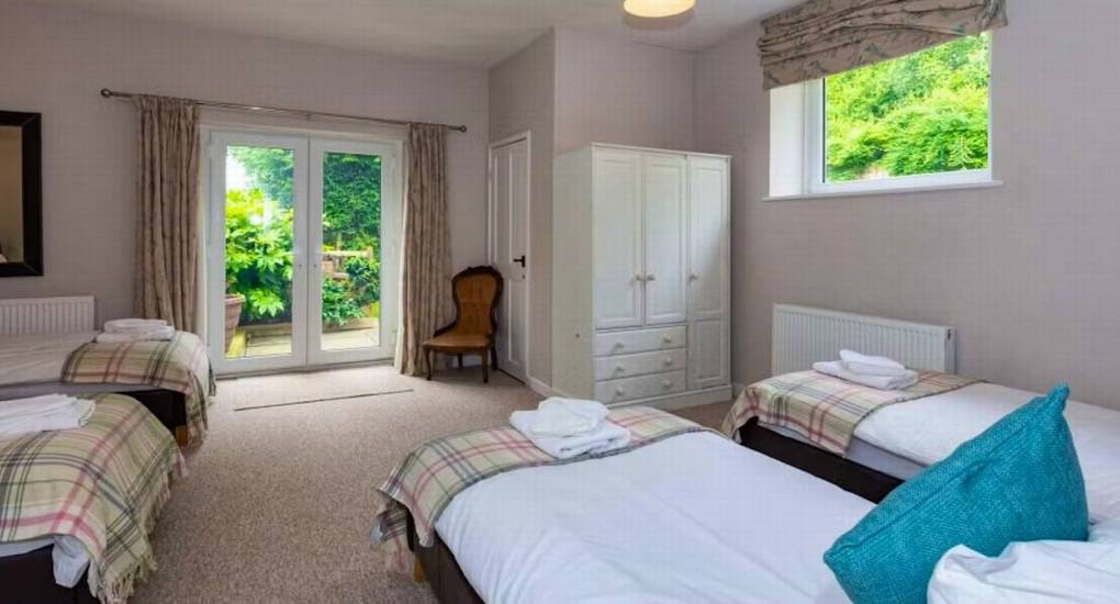 A flexible quad-sleeping bedroom at Standing Barn Gloucestershire with plaid bedspreads and French doors leading to the garden, ideal for the Party House that sleeps 22.