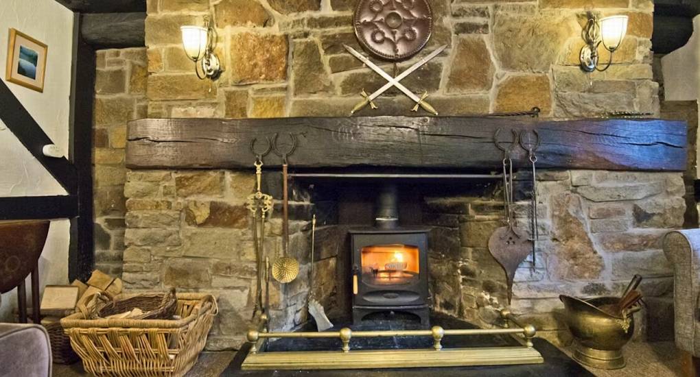 The rustic stone fireplace with a wood-burning stove and heavy timber mantel at Standing Barn Gloucestershire, adding a cozy atmosphere to this Gloucestershire Party House.