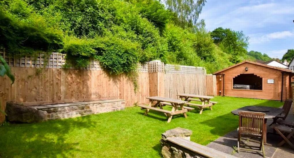 The dedicated outdoor hot tub housed in a wooden cabin, located in the grassy garden area of Standing Barn Gloucestershire, ready for the party house group.
