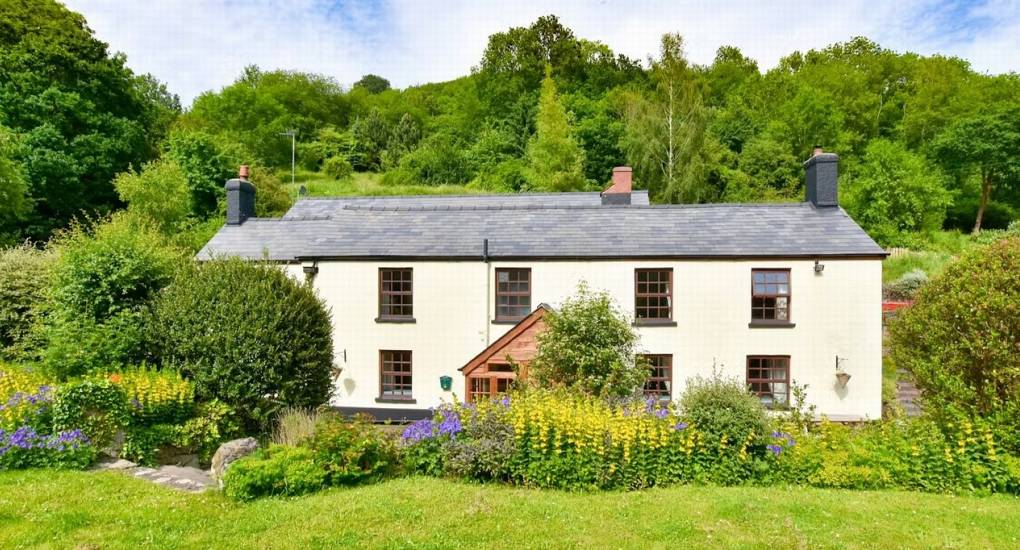 The charming white stone exterior of the Standing Barn Gloucestershire Party House, surrounded by green gardens and countryside.