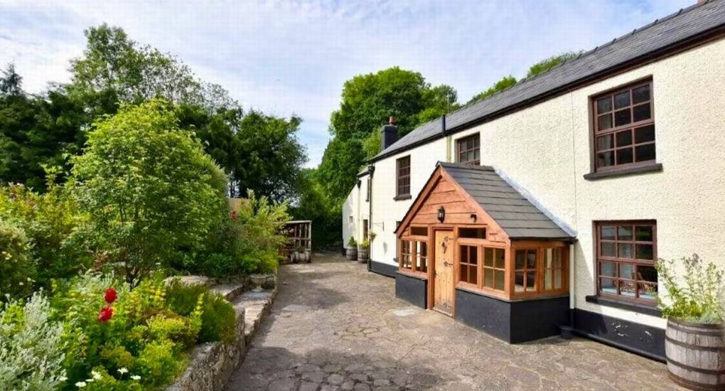 A view down the side of Standing Barn Gloucestershire, showing the wooden entrance porch and paved pathway for this Gloucestershire Party House.