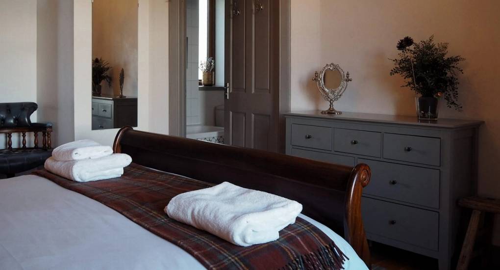 Cozy bedroom at The Lux Lodge with a dark wood sleigh bed, tartan accents, and an ensuite bathroom for a luxury Inverness hen party retreat.