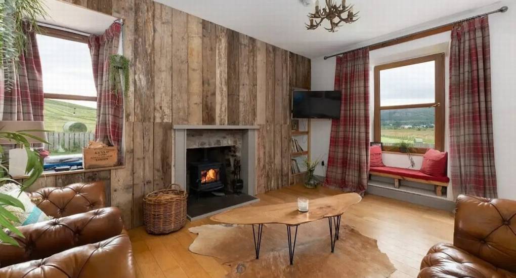 Rustic living room at The Lux Lodge featuring a roaring wood-burning stove, leather Chesterfield chairs, and an antler chandelier—ideal for an Inverness hen weekend.