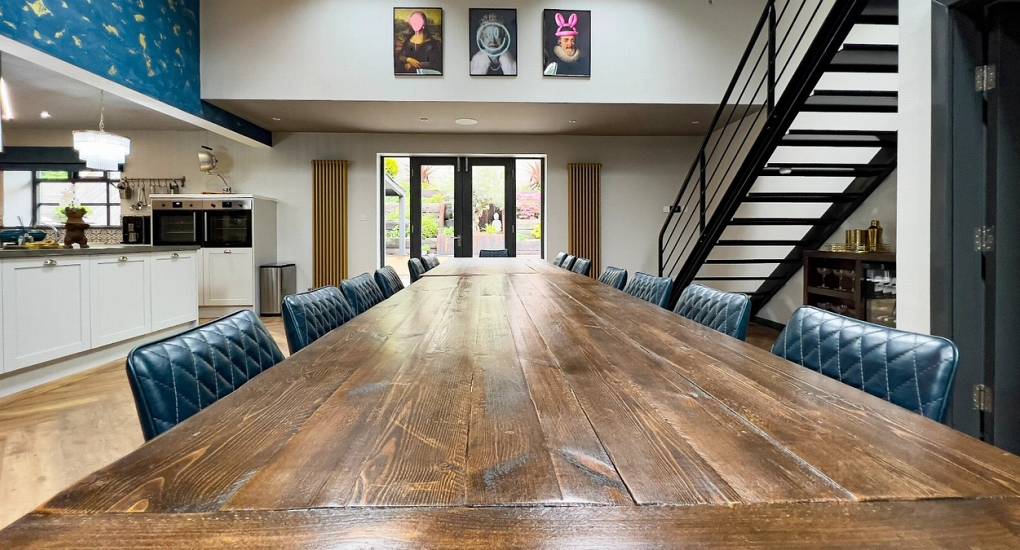 The magnificent wooden dining table at The Plush, capable of seating the whole group for a private chef dinner or murder mystery night, set against quirky modern artwork near Tynemouth.