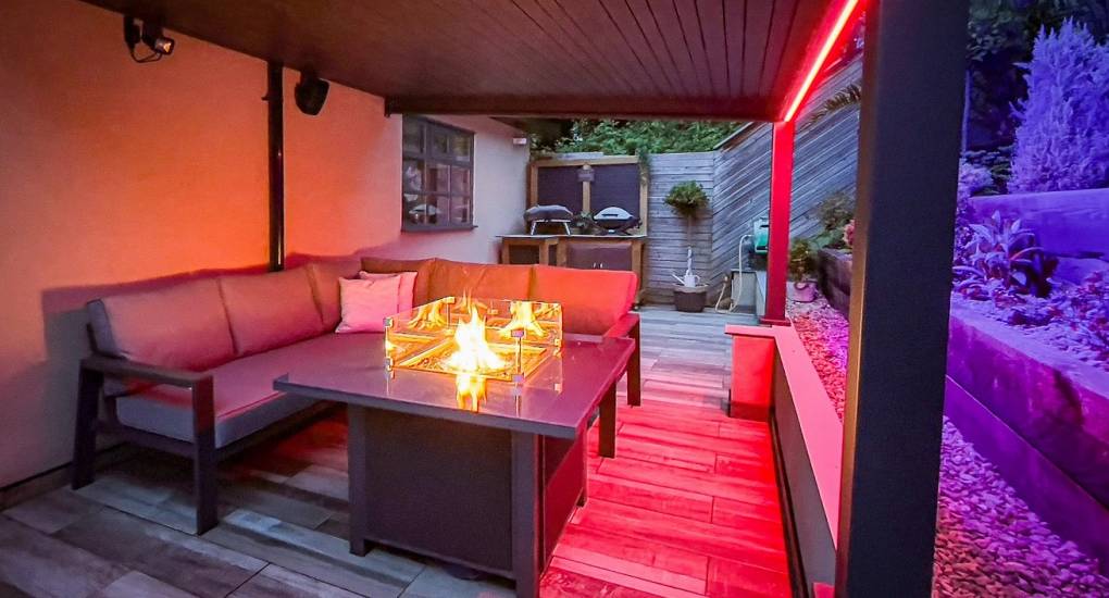 A wide view of the private outdoor social space at The Plush, a luxury Newcastle hen house, showcasing the social seating around the firepit with the two hot tubs in the background.