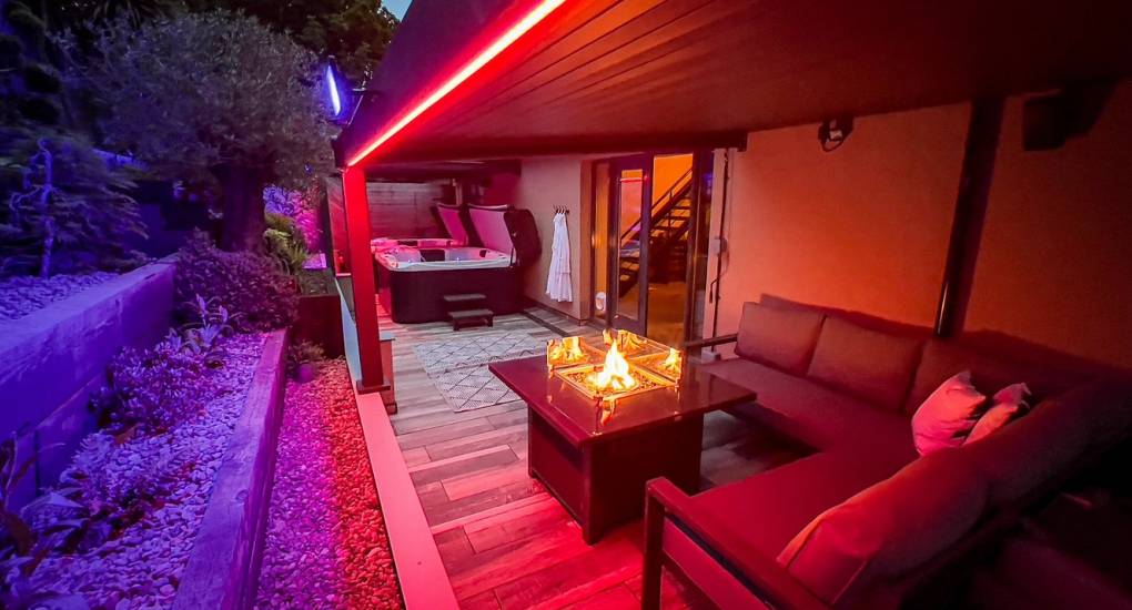 The stylish 'Garden Oasis' at The Plush near Tynemouth, featuring a cozy corner sofa and a glowing glass firepit table under atmospheric red LED lighting, perfect for evening drinks.