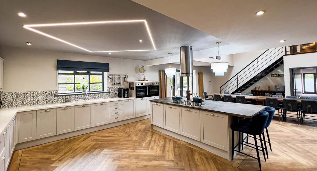 A wide-angle view of the stunning open-plan kitchen and dining hub at The Plush, a luxury Newcastle hen house, featuring high ceilings, modern cabinetry, and a spacious layout for large group socialising.