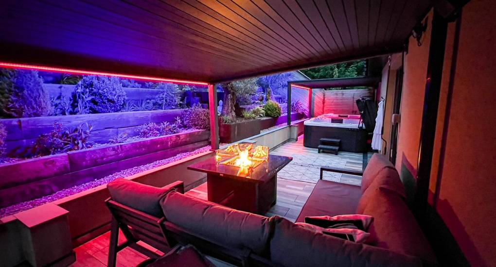 The spectacular outdoor decking area at The Plush at night, highlighting the centrally controlled mood lighting, twin hot tubs, and secluded firepit area for an upscale celebration.