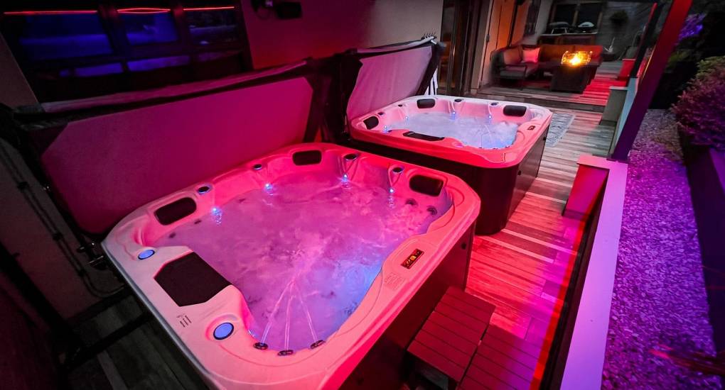 Two luxury undercover hot tubs at The Plush illuminated with vibrant pink lighting, offering a private spa experience for large groups on a glam Newcastle hen weekend.
