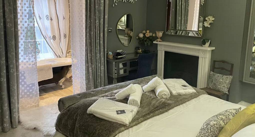 A beautiful bedroom at The Sash House featuring a double bed and a roll-top bathtub visible in the en-suite.