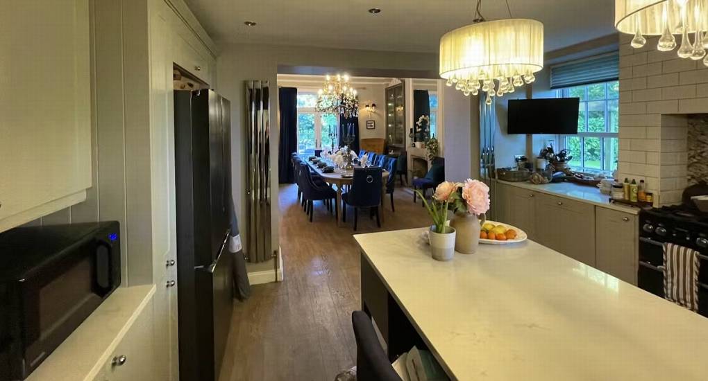 The open-plan kitchen and dining area at this hen do cottage, showing the long dining table, stylish chairs, and chandeliers.