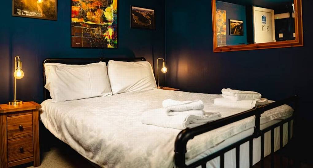 A stylish double bedroom at The Wye House with dark blue walls and modern art, providing a relaxing retreat after using the games room & hot tub.