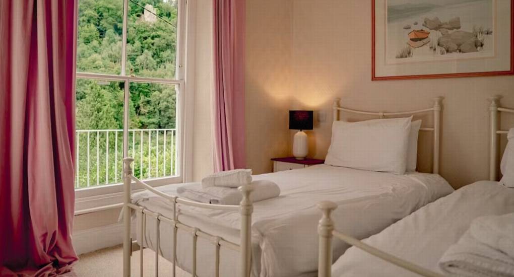 A light and airy twin bedroom at The Wye House with white metal beds and pink curtains, offering comfortable sleeping for a Herefordshire hen party.