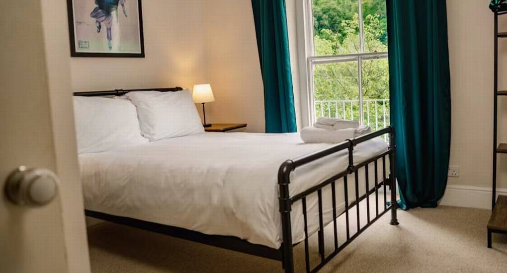 A cozy double bedroom at The Wye House featuring a black metal bed and teal curtains, one of several rooms that allow the property to sleep 22.