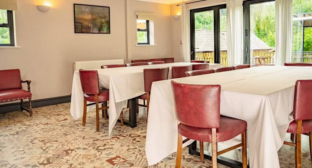 The spacious dining room at The Wye House with large tables and red leather chairs, set up to comfortably seat the full hen party group that sleeps 22 for a celebration meal at the Herefordshire hen party house.