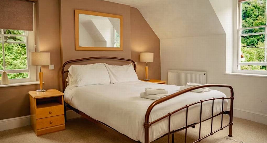 A light and airy twin bedroom at The Wye House with white metal beds and pink curtains, offering comfortable sleeping for a Herefordshire hen party.