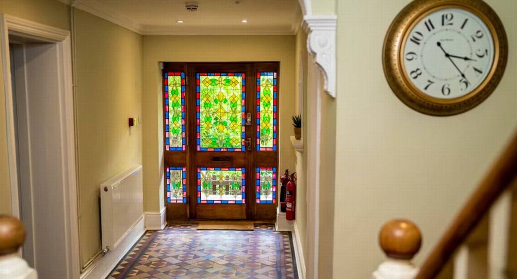 The welcoming entrance hallway at The Wye House featuring a traditional patterned floor and a stunning stained glass front door, offering a grand arrival for this Herefordshire hen party house.