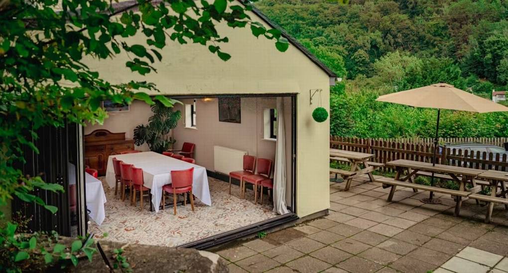 A view from the outside patio looking through open bi-fold doors into the spacious dining area of The Wye House, which is ideal for a large Herefordshire hen party that sleeps 22.
