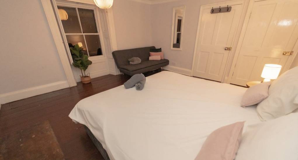 A spacious double bedroom at Tranquil Escape, a rural Newcastle hen do house, featuring original dark wood flooring and a grey sofa bed to accommodate larger groups.