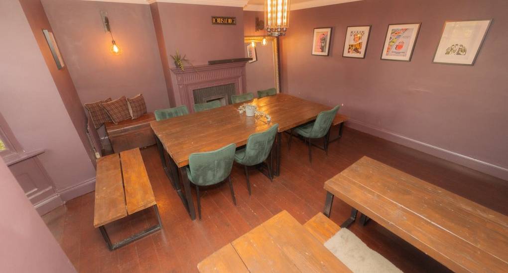 The spacious dining room at Tranquil Escape, a rural Newcastle hen do house, featuring multiple rustic wooden tables and green velvet seating, ideal for large group dinners and in-house activities like murder mystery nights.
