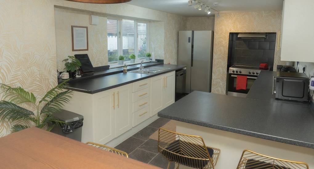 The modern white kitchen at Tranquil Escape, a rural Newcastle hen do house, featuring a large American-style fridge freezer, gold hardware, and ample counter space for group catering.