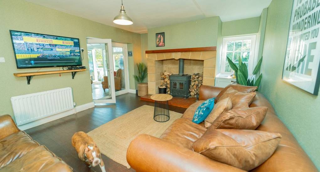 The cozy lounge at Tranquil Escape, a rural Newcastle hen do house, featuring charismatic weathered leather sofas, a traditional log burner fireplace, and a large wall-mounted TV for group movie nights.