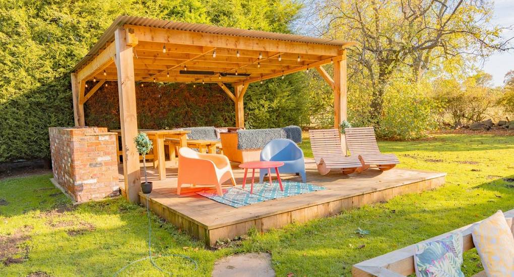 A stylish wooden pergola and private garden bar at Tranquil Escape, featuring lounge seating, colorful decor, and festoon lighting—perfect for a sunny afternoon Newcastle hen do.