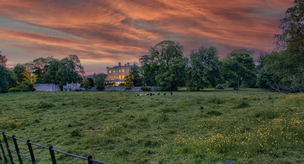 View of the Country Fortress hen party house from across a field at dusk with the lights on at the manor house