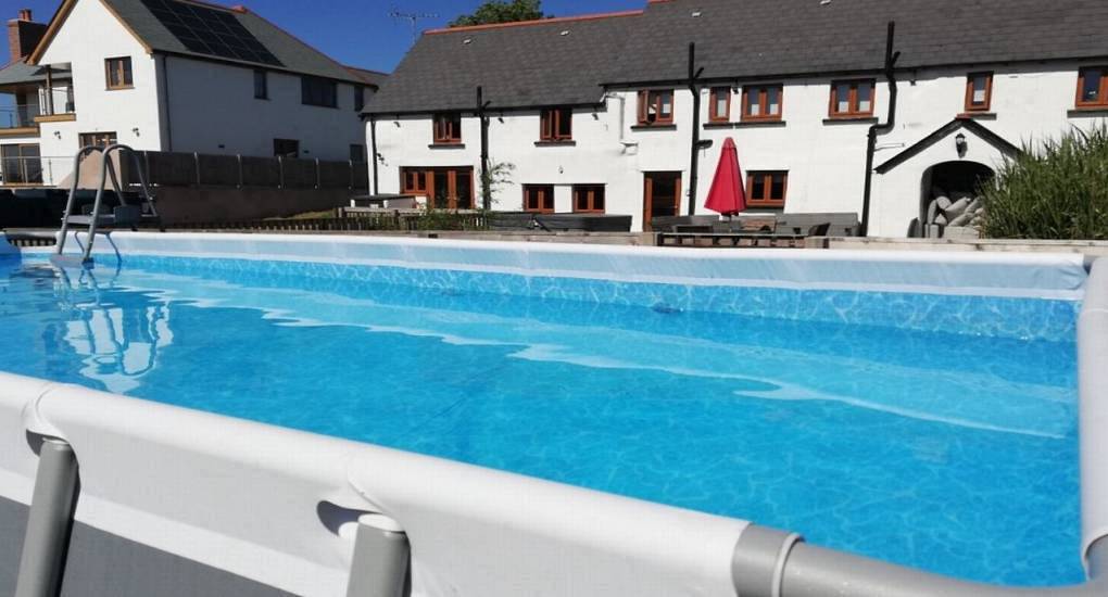 The outdoor swimming pool and white holiday cottages at Devon Barns, a North Devon hen party barn for large groups.