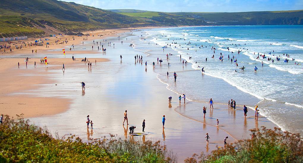 Crowds and surfers enjoying golden sand and waves at Woolacombe Beach, sunny coastal setting for a Woolacombe hen do.