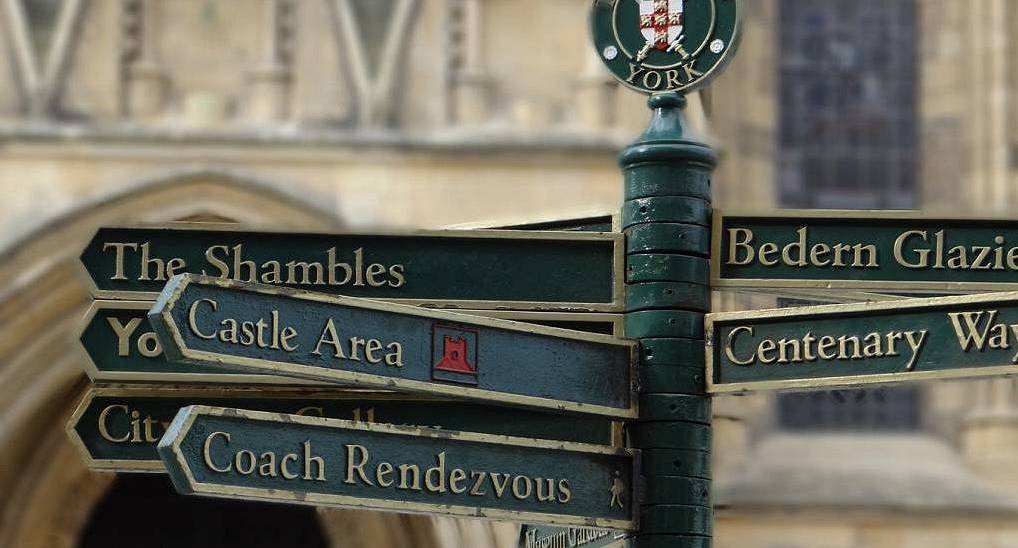 Traditional green metal signpost pointing to The Shambles and Castle Area in York, historic backdrop for a York stag do.