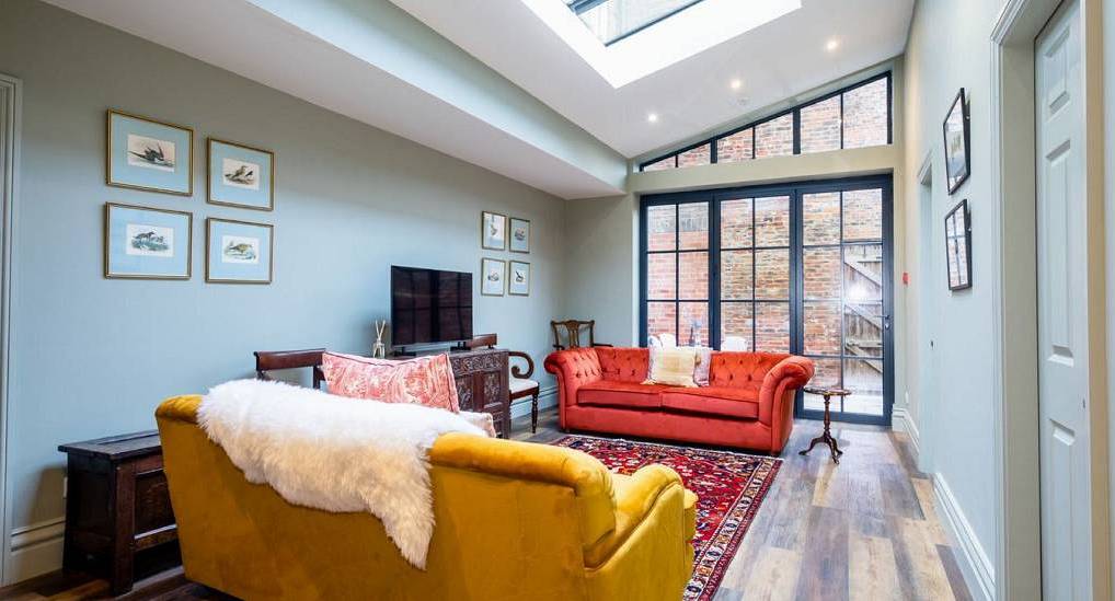 The skylight lounge with yellow and velvet orange sofas at York Treat, a characterful central York hen townhouse for 12.